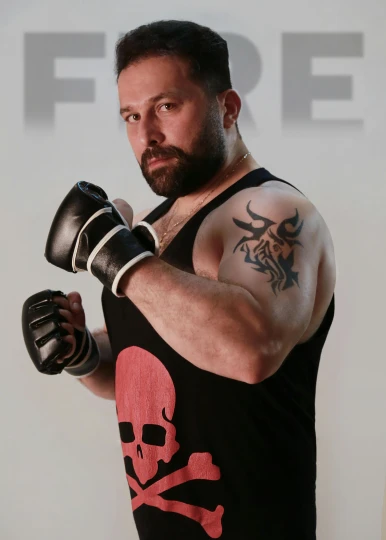 a man wearing a tank top with a skull and crossbone on it, inspired by ken kelly, boxing gloves, body of pure fire, promo photo, bearded and built
