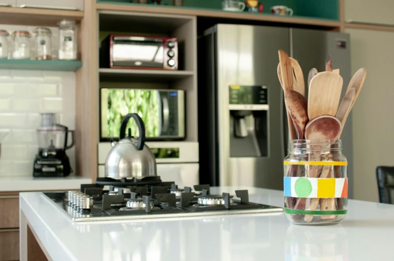 a glass jar filled with wooden utensils on top of a kitchen counter, by Felipe Seade, pexels contest winner, colorful accents, tv still, stainless steal, yellow and green scheme