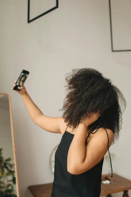 a woman standing in front of a mirror holding a camera, trending on pexels, happening, long afro hair, hold up smartphone, hands in her hair. side-view, flat ironed hair