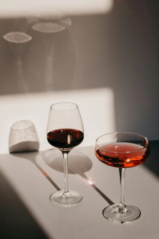 a couple of wine glasses sitting on top of a table, a still life, pexels contest winner, purism, mangeta smoke red light, midcentury modern, on a white table, detailed product shot