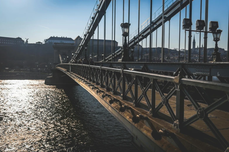 a bridge over a body of water with buildings in the background, by Matija Jama, pexels contest winner, modernism, hungarian, slightly sunny, thumbnail, metallic bridge