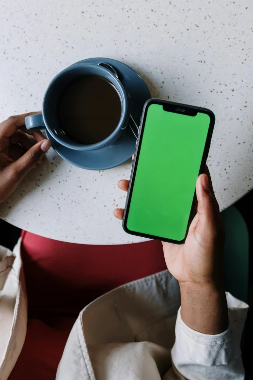 a person sitting at a table holding a phone with a green screen, trending on pexels, coffee, 2 5 6 x 2 5 6 pixels, ( ( dark skin ) ), no - text no - logo