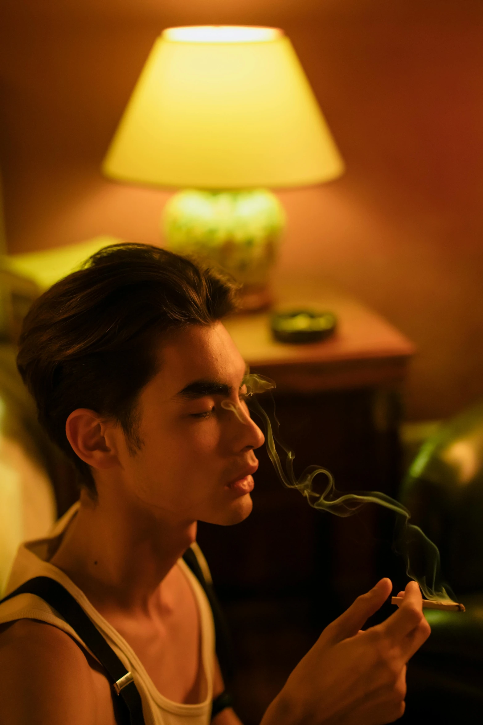 a man smokes a pipe in a dimly lit room, inspired by Zhang Han, trending on pexels, 18 years old, 8 k sensual lighting, movie still, lush surroundings