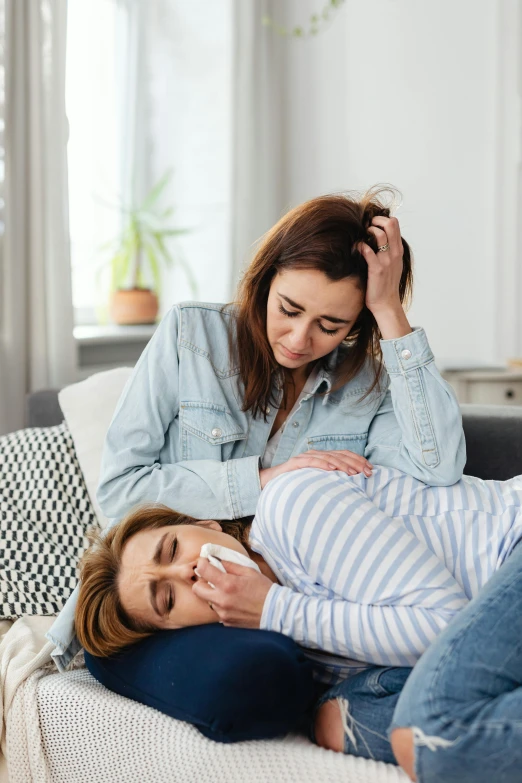 a couple of women laying on top of a couch, a picture, by Julia Pishtar, trending on pexels, coughing, medical, maternal, with a hurt expression