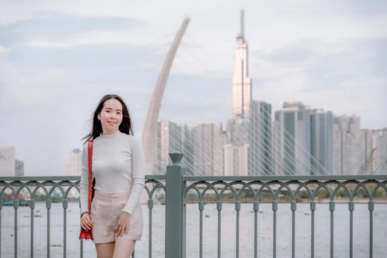 a woman standing on a bridge with a city in the background, inspired by Cheng Jiasui, pexels contest winner, background image, vietnamese woman, group photo, view(full body + zoomed out)