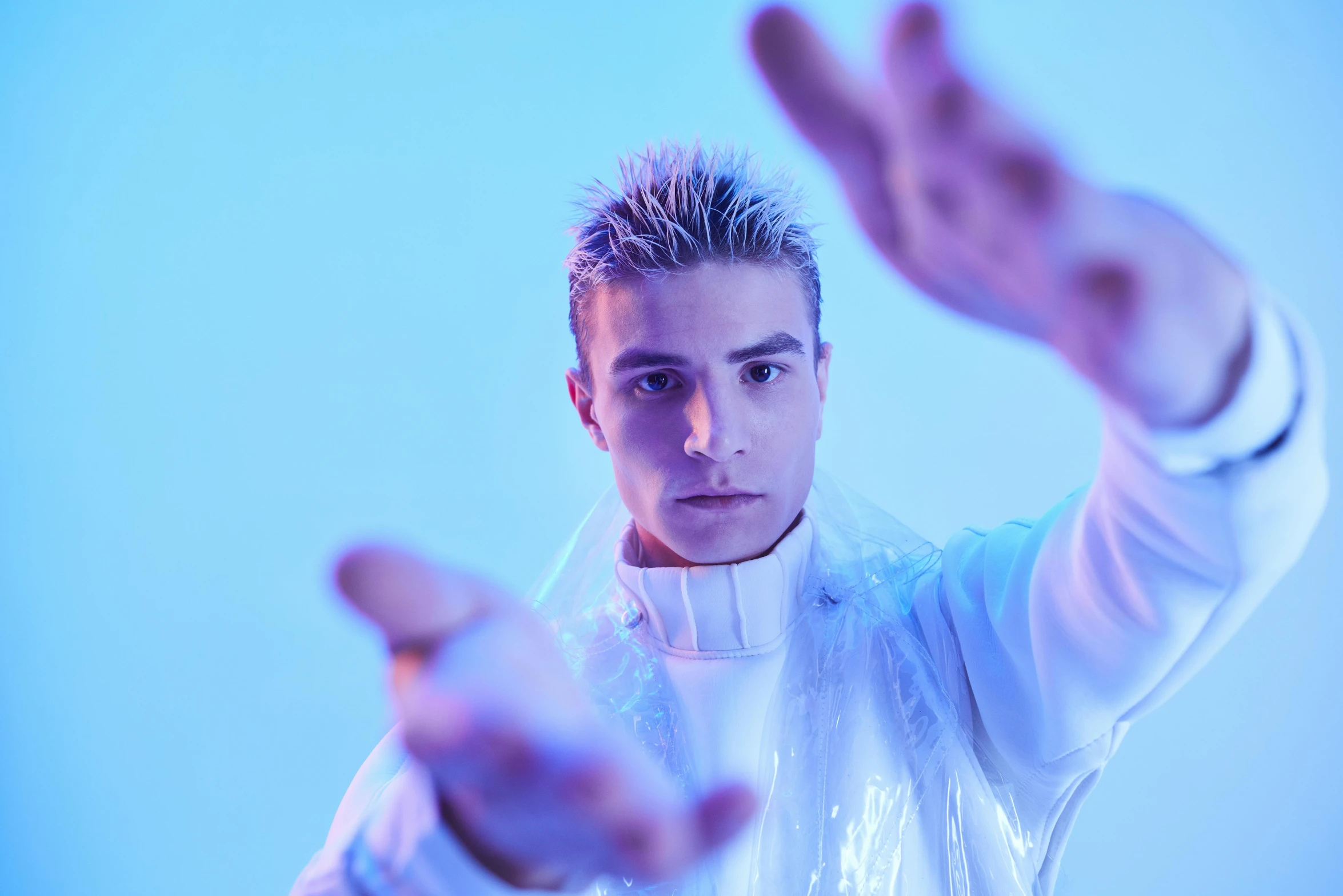 a man standing in front of a blue background, an album cover, inspired by Kristian Kreković, in white futuristic armor, behind the scenes photo, promo still, portrait image
