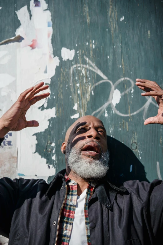 a man with his hands up in the air, black arts movement, grey beard, hand on cheek, spraypainted on a wall, in distress