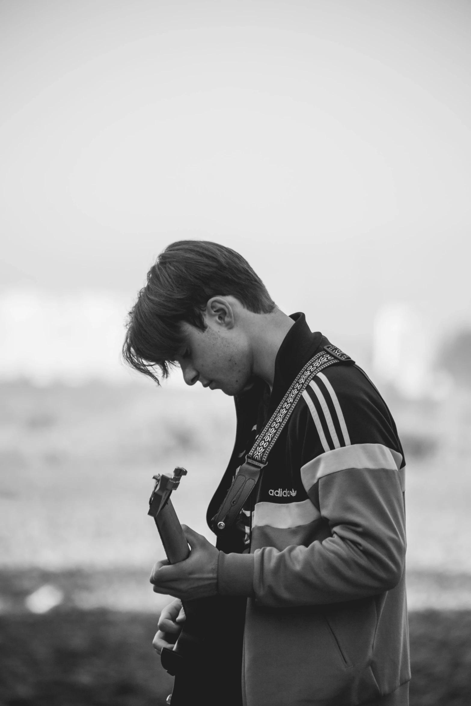 a man standing on top of a beach next to the ocean, a black and white photo, unsplash, realism, playing a mandolin, declan mckenna, holding a wrench, he is sad