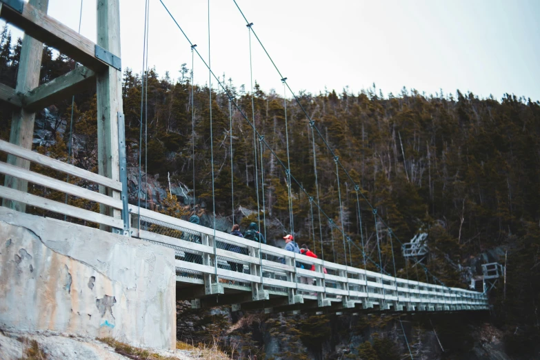 a couple of people that are standing on a bridge, by Jessie Algie, pexels contest winner, large overhangs, quebec, 2 5 6 x 2 5 6 pixels, hanging cables