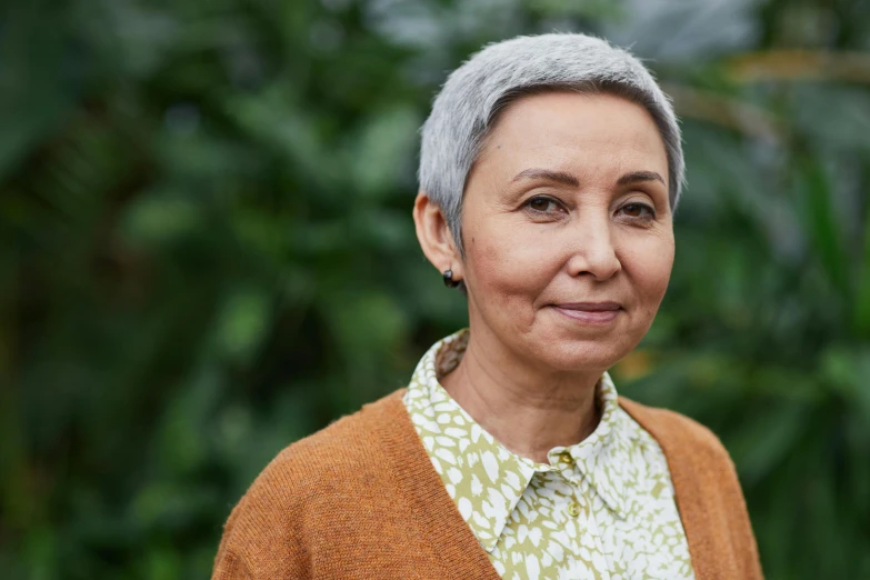 a close up of a person wearing a sweater, a portrait, by Helen Stevenson, pexels contest winner, hurufiyya, short grey hair, standing in a botanical garden, mixed race woman, portrait of a female pathologist