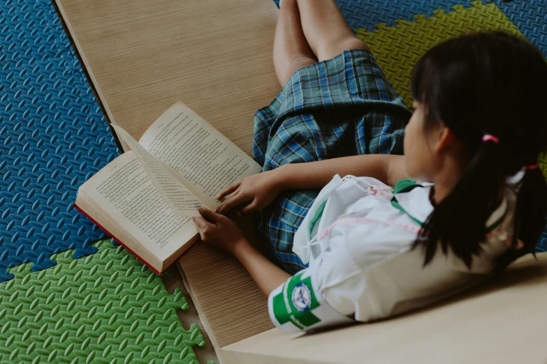 a little girl is reading a book on the floor, inspired by Béni Ferenczy, pexels contest winner, girl wearing uniform, sustainable materials, avatar image, gemma chen