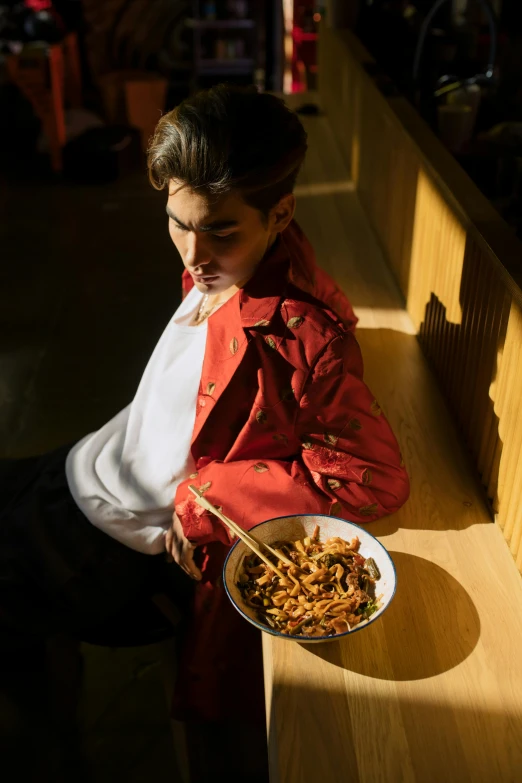 a woman sitting on a bench holding a bowl of food, androgynous male, cool red jacket, pasta, intense lighting