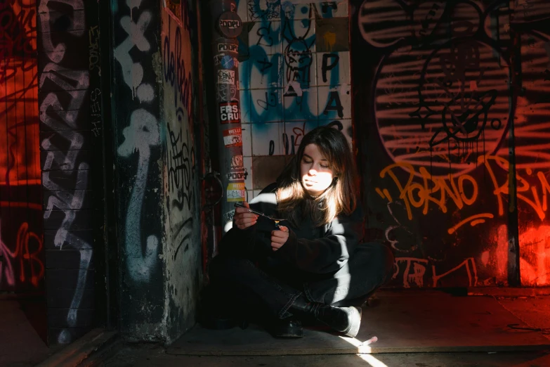 a woman sitting on the ground in front of a wall covered in graffiti, inspired by Elsa Bleda, pexels contest winner, maisie williams, selfie photo, good lighted photo, in a claustrophobic