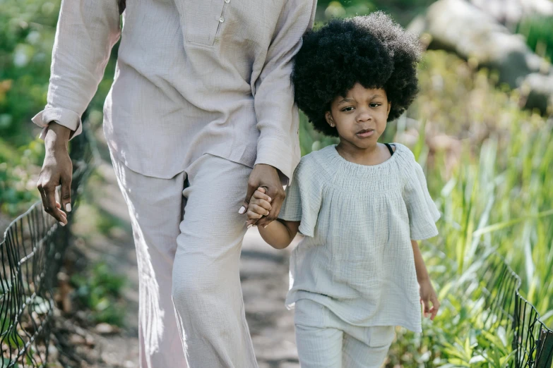 a woman and a child walking down a path, by Lily Delissa Joseph, pexels, symbolism, long afro hair, grayish, toddler, green and brown clothes