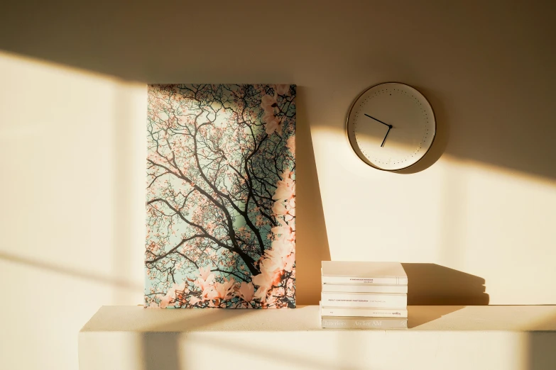 a clock sitting on top of a white shelf next to a painting, a detailed painting, inspired by Elsa Bleda, unsplash, generative art, cherry blossom tree, earthy light pastel colours, angle view, blue woodcut print