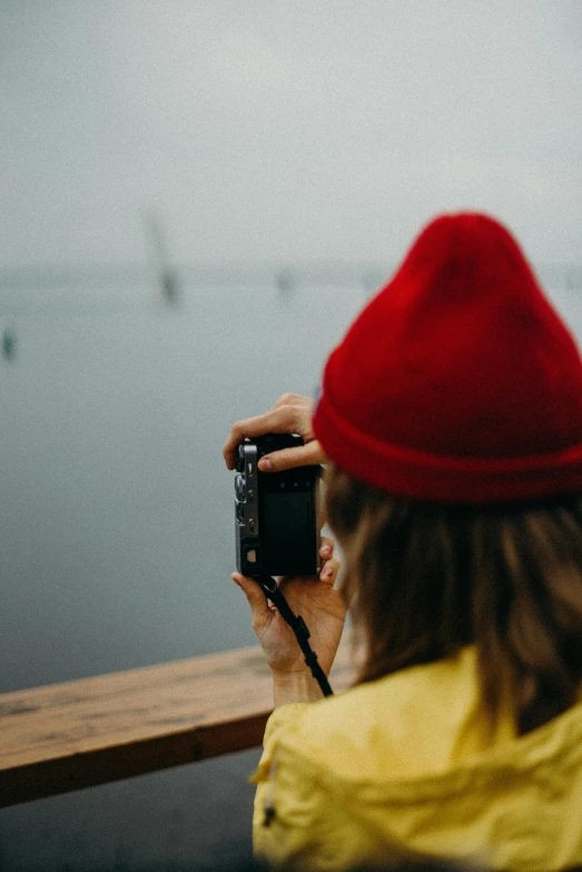 a person taking a picture of a body of water, red hat, camera looking up at her, 2019 trending photo, portrait photo