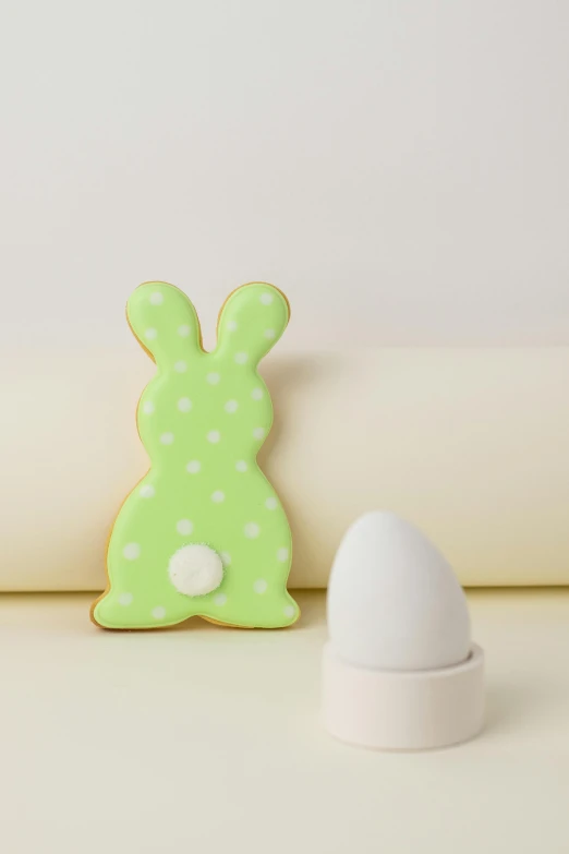 a cookie sitting on top of a table next to an egg, light green, polka dot, bunny, product shot