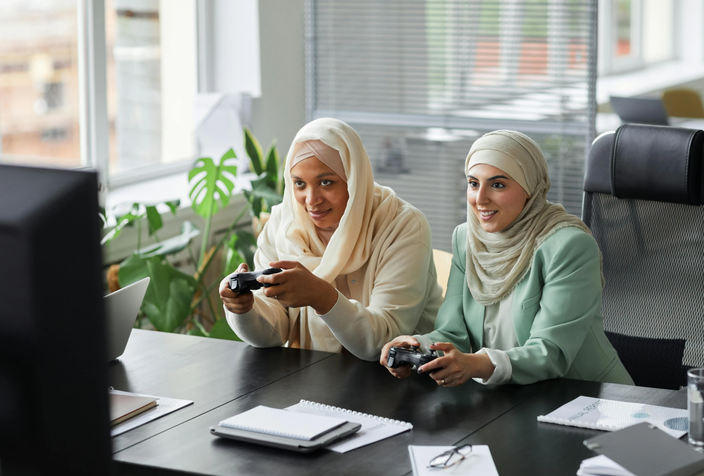 two women sitting at a table playing video games, inspired by Charly Amani, hurufiyya, coworkers, islamic, woman holding another woman, medium-shot