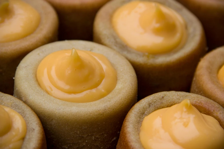 a close up of a tray of cupcakes with frosting, inspired by Géza Dósa, mingei, yellow-orange, inside a cavernous stomach, cone shaped, flan