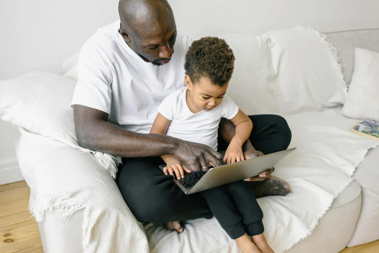 a man and a child sitting on a couch with a laptop, by Carey Morris, pexels, black, toddler, performing, maintenance