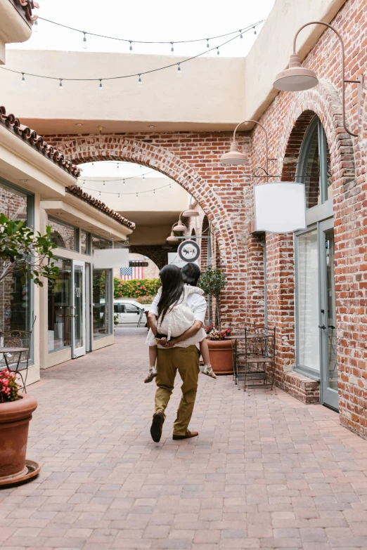 a man with a backpack walking down a brick walkway, by Julia Pishtar, the city of santa barbara, couple dancing, exiting store, white sweeping arches