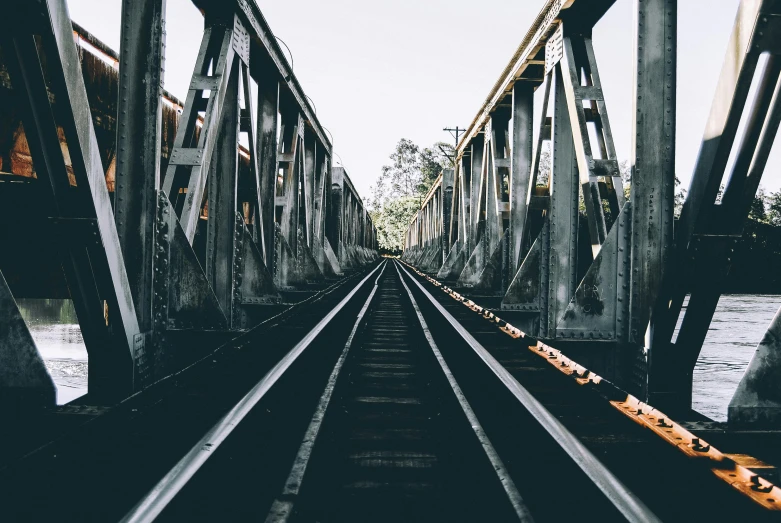 a train track going over a bridge next to a body of water, an album cover, unsplash contest winner, worksafe. instagram photo, vsco film grain, postapocalyptic vibes, crossing the line