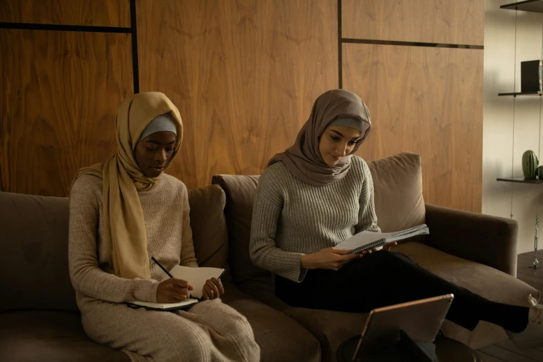 a couple of women sitting on top of a couch, by Maryam Hashemi, trending on pexels, hurufiyya, holding notebook, school class, muslim, muted browns