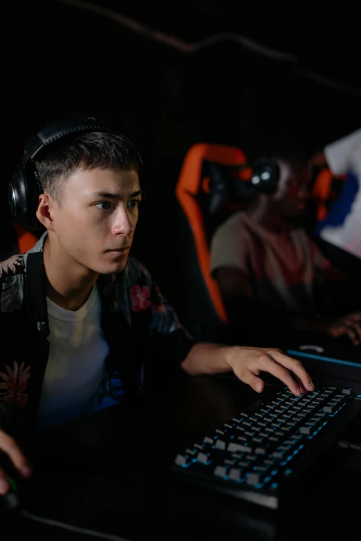 a man wearing headphones sitting in front of a computer, the video game, malaysian, on a dark background, looking serious