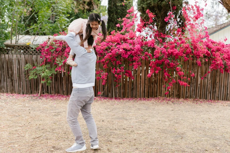 a woman holding a baby in her arms, pexels contest winner, figuration libre, bougainvillea, daddy/fatherly, walking at the garden, gray