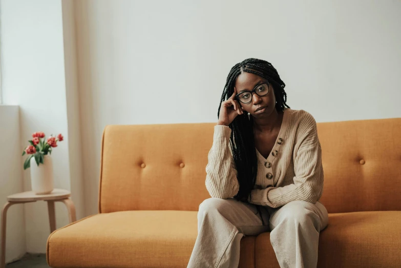 a woman sitting on a couch talking on a cell phone, a portrait, by Lily Delissa Joseph, trending on pexels, with square glasses, ashteroth, sad and lonley, on a couch