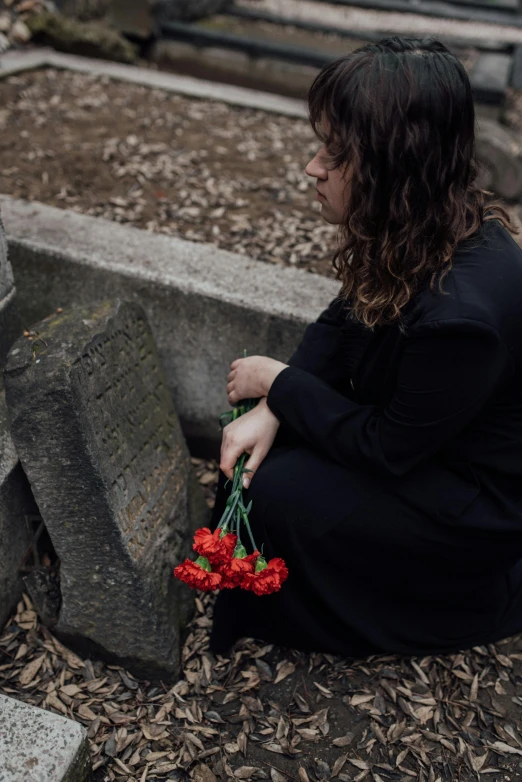 a woman sitting in front of a grave holding a bunch of flowers, unsplash, wearing a black and red suit, facing away, ignant, profile image