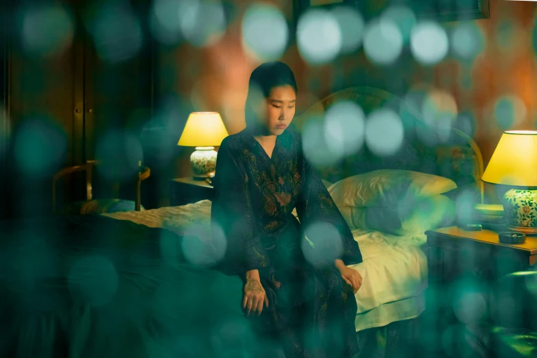 a woman sitting on a bed in a room, an album cover, inspired by Tang Yin, pexels contest winner, movie still of a tired, brooding, cinestill colour cinematography, bokeh top cinematic lighting