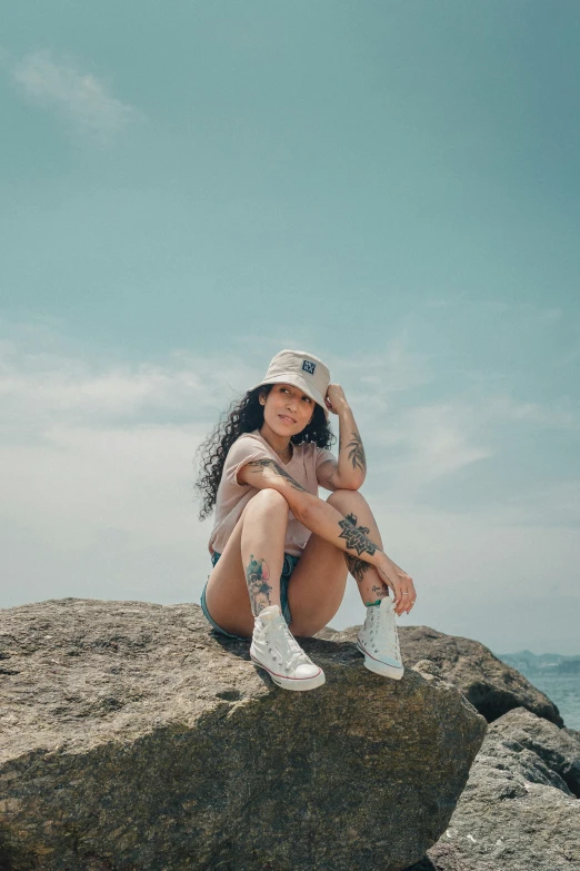 a woman sitting on top of a rock next to the ocean, bra and shorts streetwear, wearing a baseball hat, avatar image, wearing white sneakers