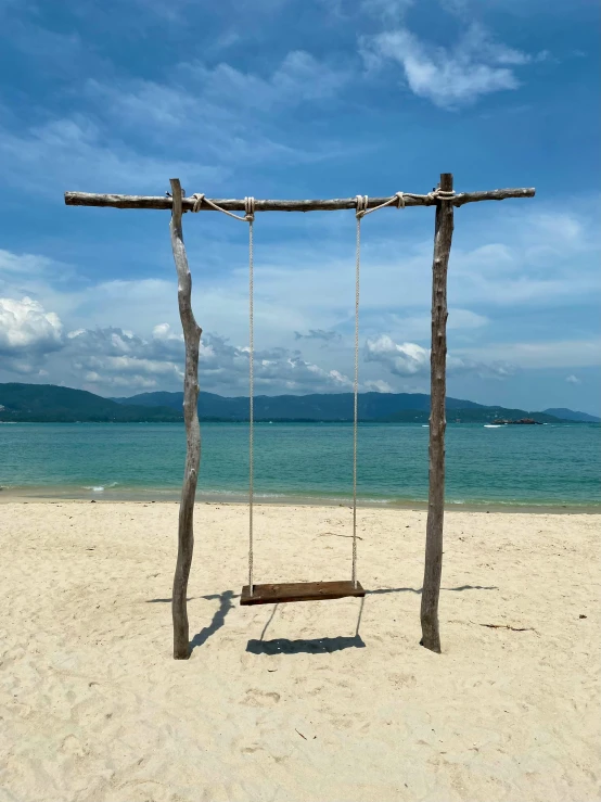 a wooden swing sitting on top of a sandy beach, in style of thawan duchanee, square, lisa kristine