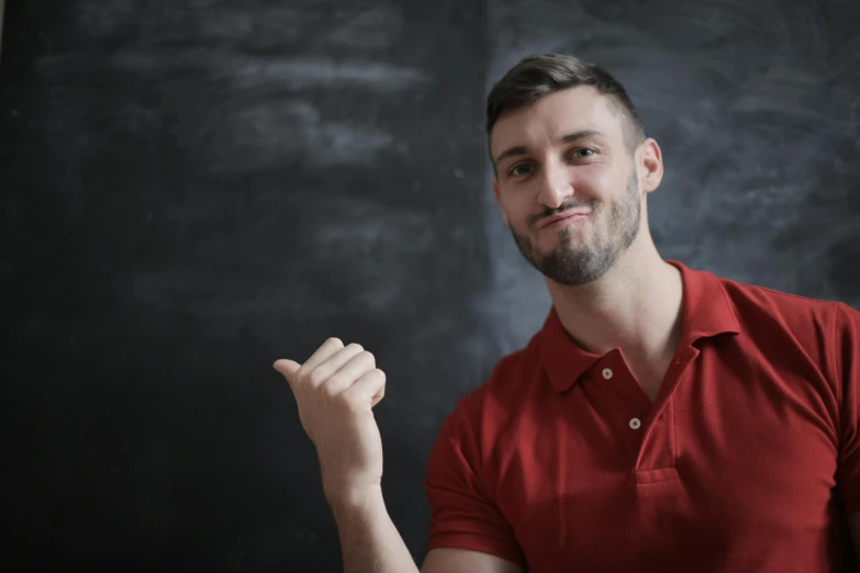a man in a red shirt standing in front of a blackboard, pexels contest winner, with index finger, square masculine jaw, young man with medium - length, h3h3