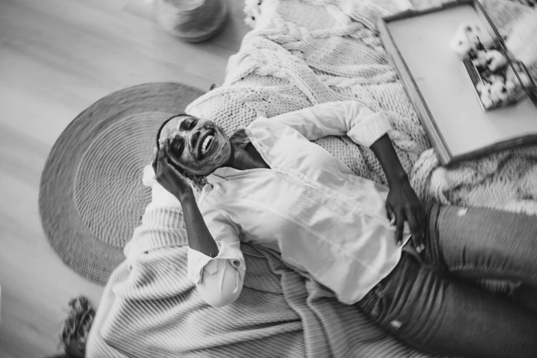 a black and white photo of a man laying on a couch, a black and white photo, by Emma Andijewska, pexels, brown skin man with a giant grin, white shirt and jeans, a high angle shot, african woman