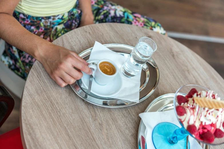 a person sitting at a table with a plate of food, two cups of coffee, turquoise and venetian red, silver small small small glasses, cold brew coffee )