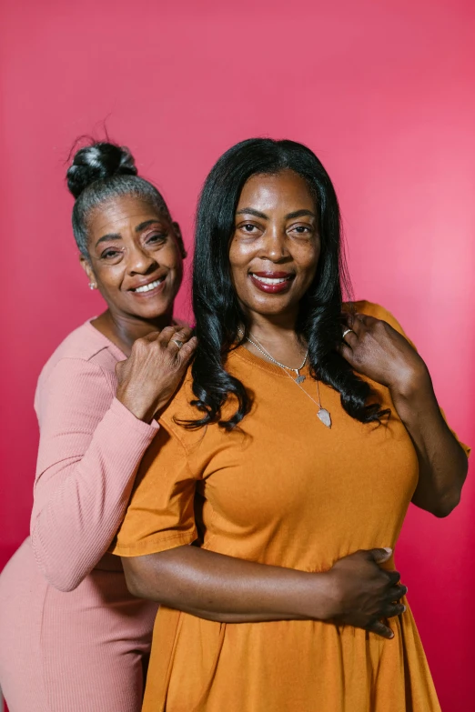 two women standing next to each other in front of a red background, motherly, dark skinned, high-quality photo, square