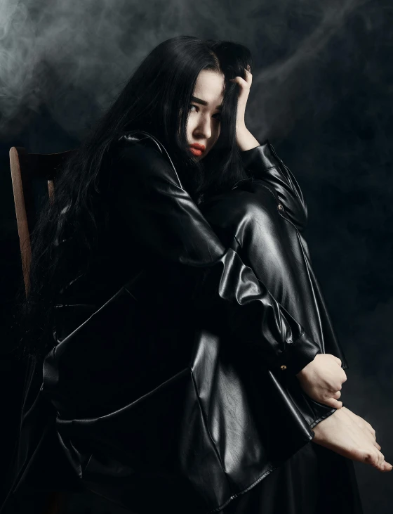 a woman in a black leather jacket sitting on a chair, an album cover, inspired by Wang E, unsplash, brooding, profile image, long black hair, spooky photo