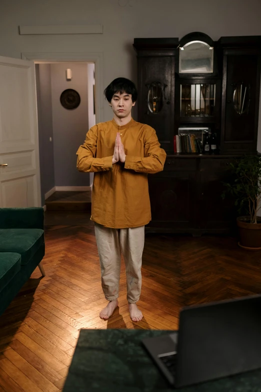 a man standing in a living room next to a laptop, inspired by Gong Kai, unsplash, renaissance, centered full body pose, yellow robe, wearing a track suit, asian human