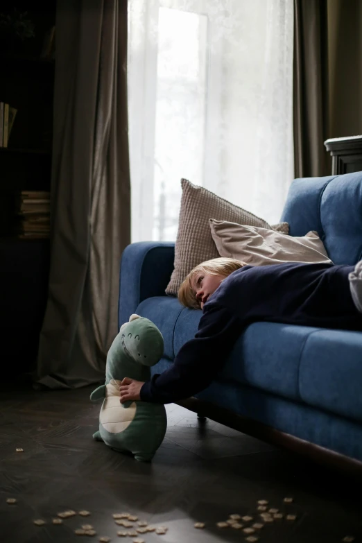 a little boy laying on a couch with a stuffed animal, inspired by Sarah Lucas, unsplash, light green and deep blue mood, teenage girl, jörmungandr, plush furnishings