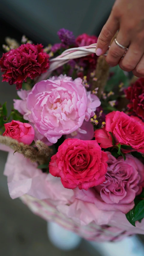 a close up of a person holding a basket of flowers, pinks, peony, magenta colours, bustling