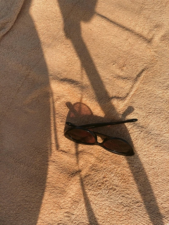 a pair of sunglasses sitting on top of a sandy beach, a picture, shadow play, taken on iphone 1 3 pro, sun puddle, brown ) )