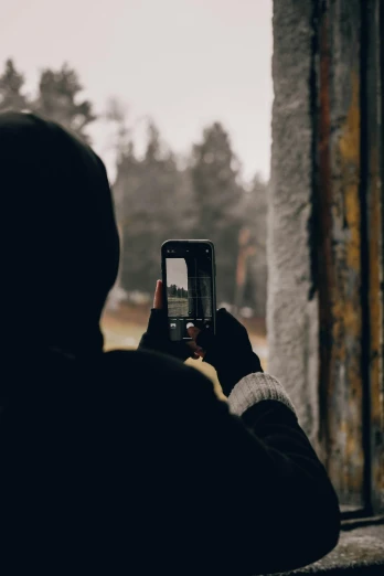 a person taking a picture with a cell phone, pexels contest winner, wearing jeans and a black hoodie, looking outside, winter photograph, faded worn