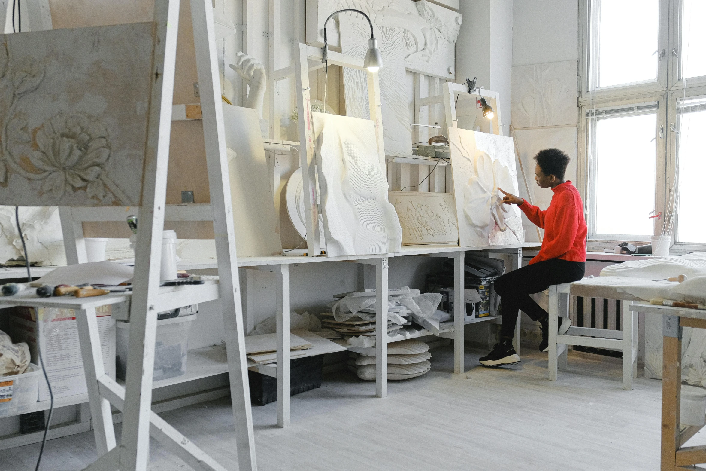 a woman sitting at a table working on a piece of art, a marble sculpture, arbeitsrat für kunst, inside a grand studio, red and white marble panels, white wall coloured workshop, jean - baptiste belin