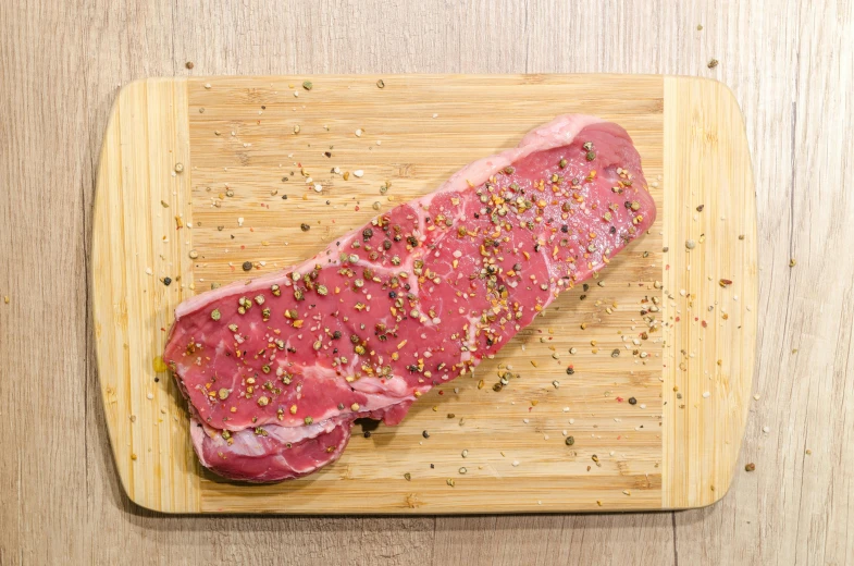 a piece of meat sitting on top of a wooden cutting board, a picture, during the day, speckled, overview, illustration »