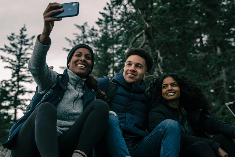 three people sitting on a rock taking a selfie, pexels contest winner, happening, movie promotional image, diverse, black, smiling