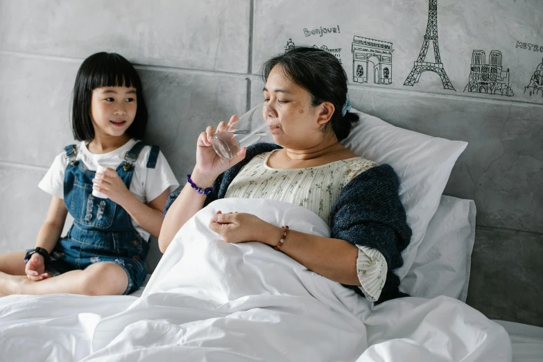 a woman sitting on top of a bed next to a little girl, inspired by Ruth Jên, pexels contest winner, drinking cough syrup, singapore, filled with water, profile image