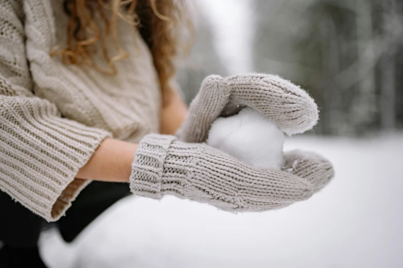 a woman holding a snowball in her hands, by Emma Andijewska, pexels contest winner, light grey, mittens, thumbnail, background image