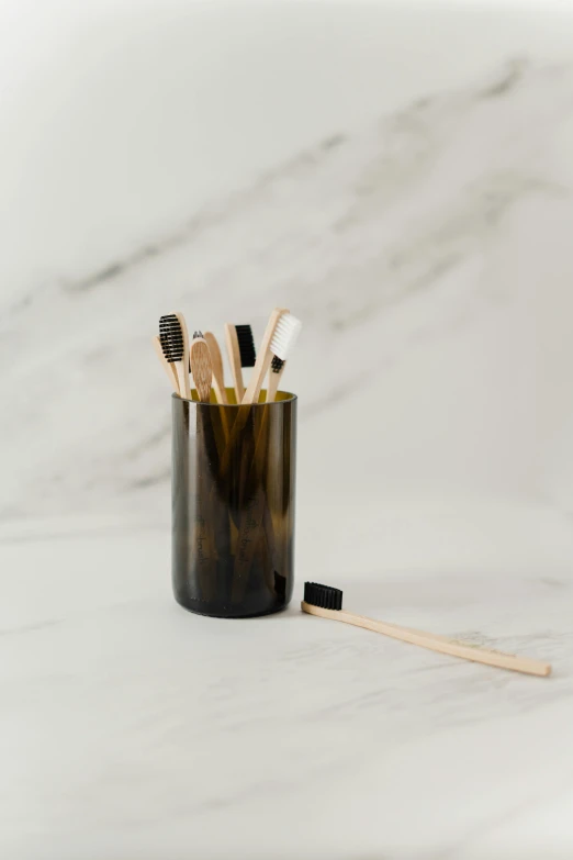 a toothbrush holder sitting on top of a marble counter, by Jessie Algie, muted brown yellow and blacks, bamboo, on clear background, charcoal